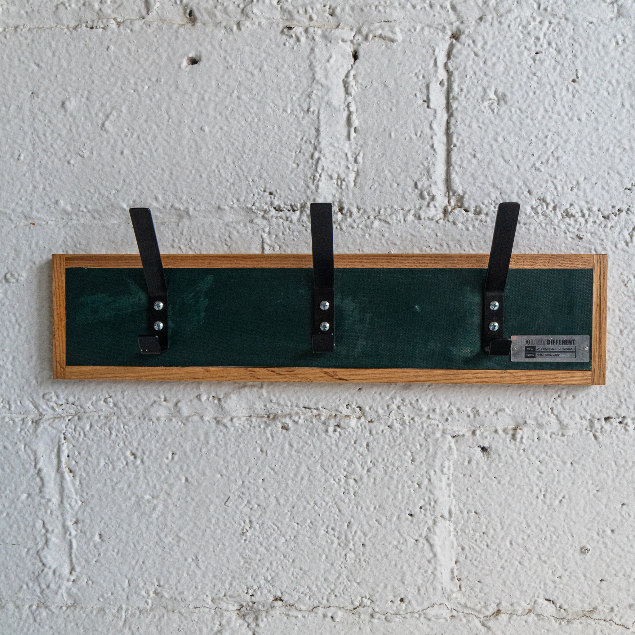Wall-mounted coat rack with green hooks against a white brick wall