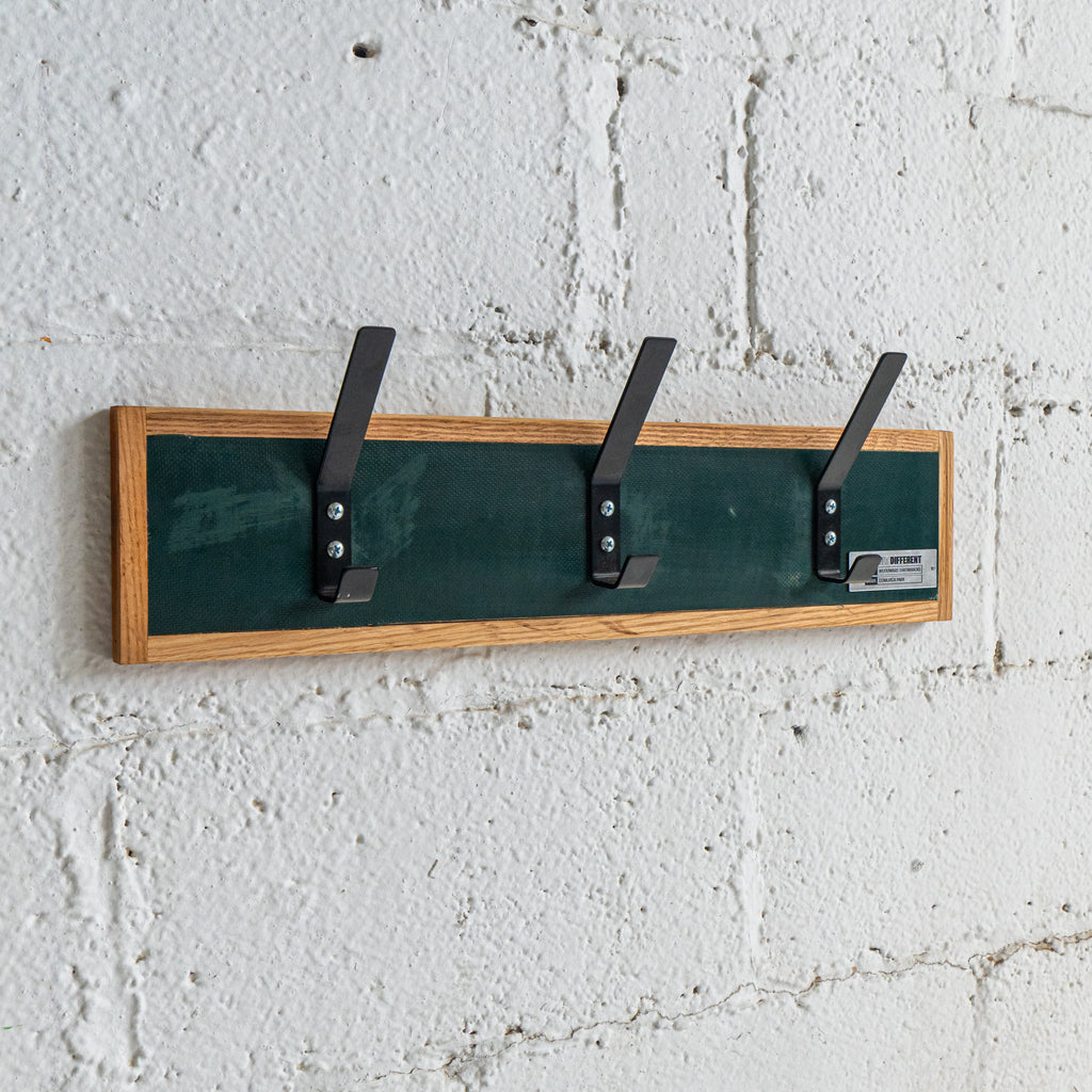 Wall-mounted coat rack with three hooks on a textured white wall.