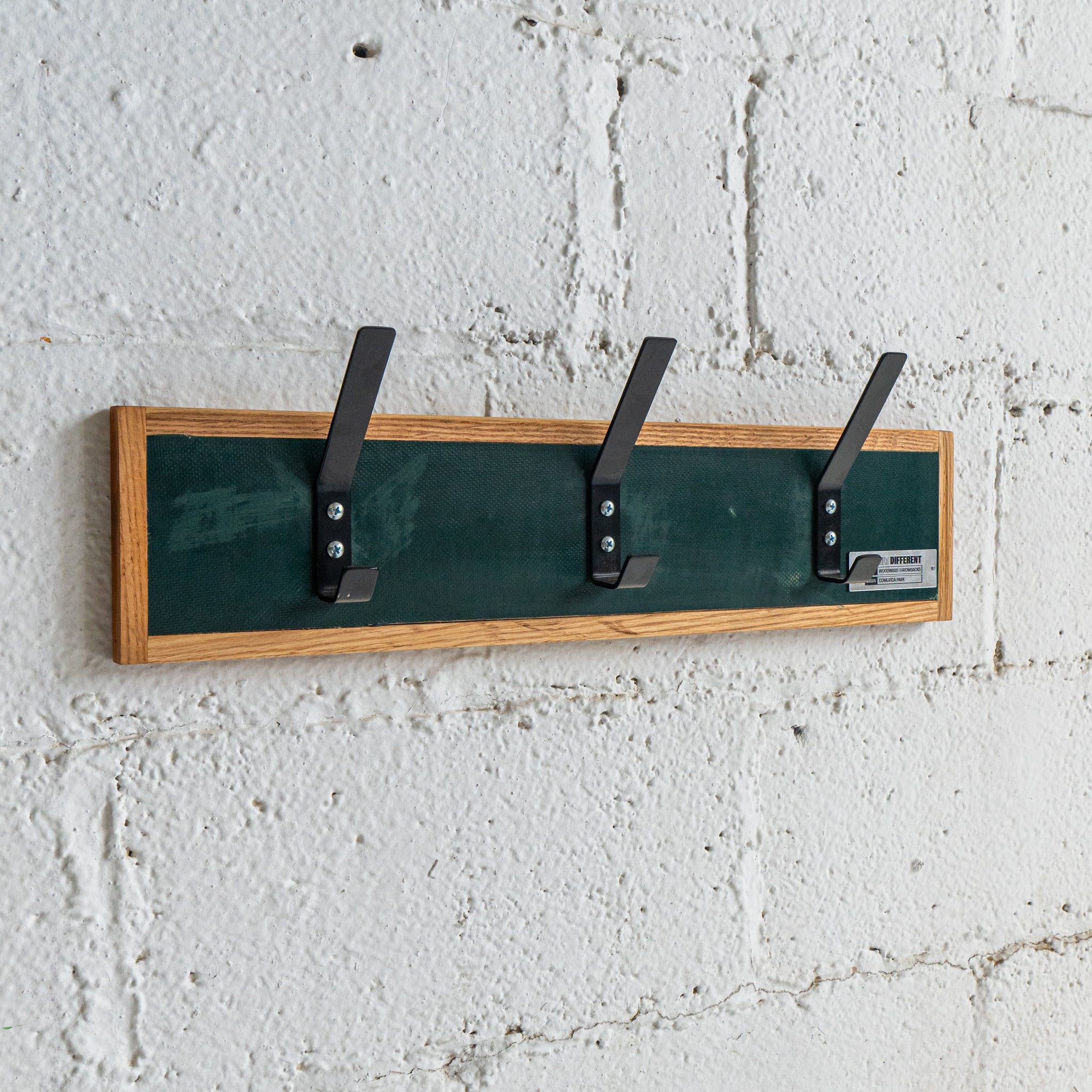 Wall-mounted coat rack with three hooks on a textured white wall.