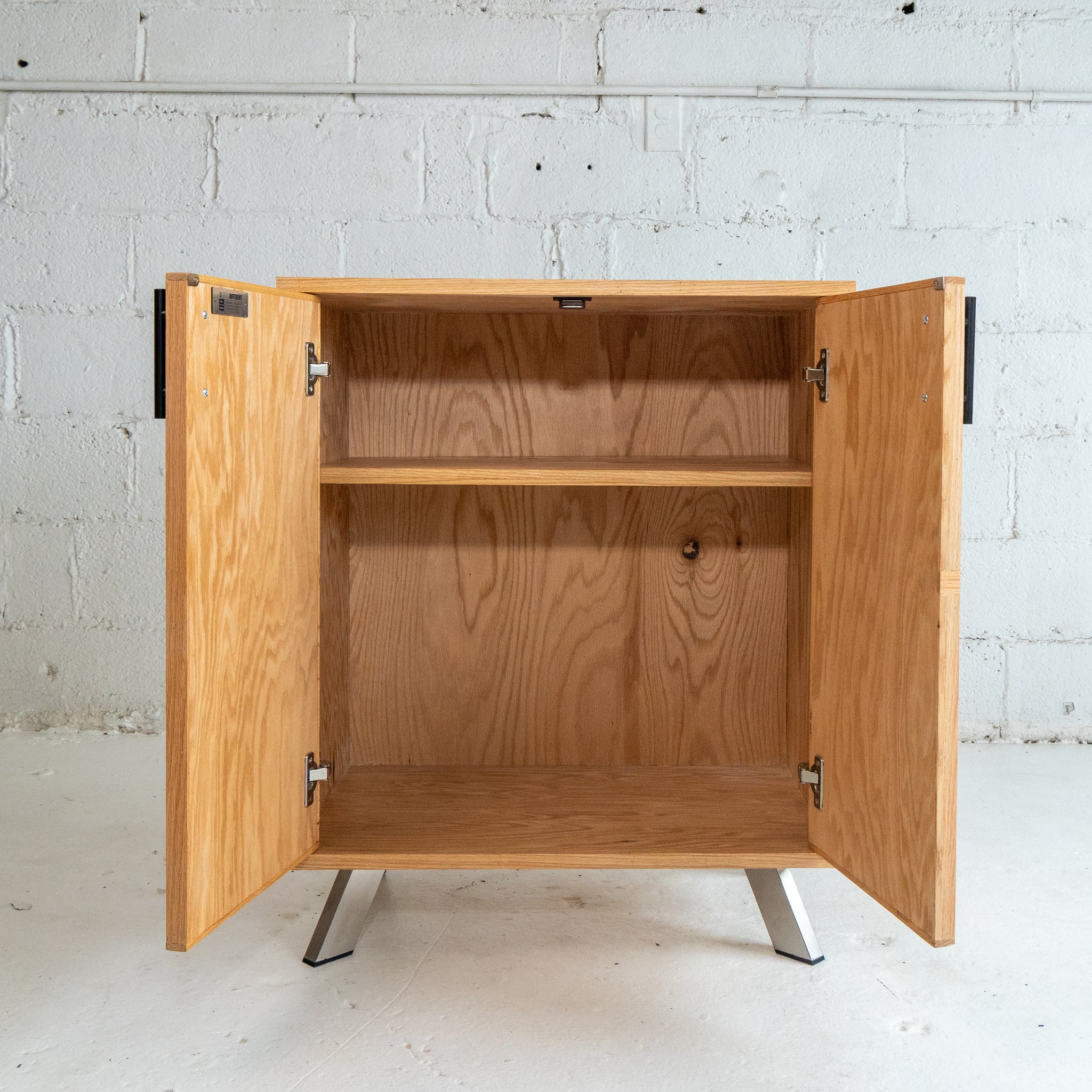 Wooden cabinet with open doors against a gray brick wall.