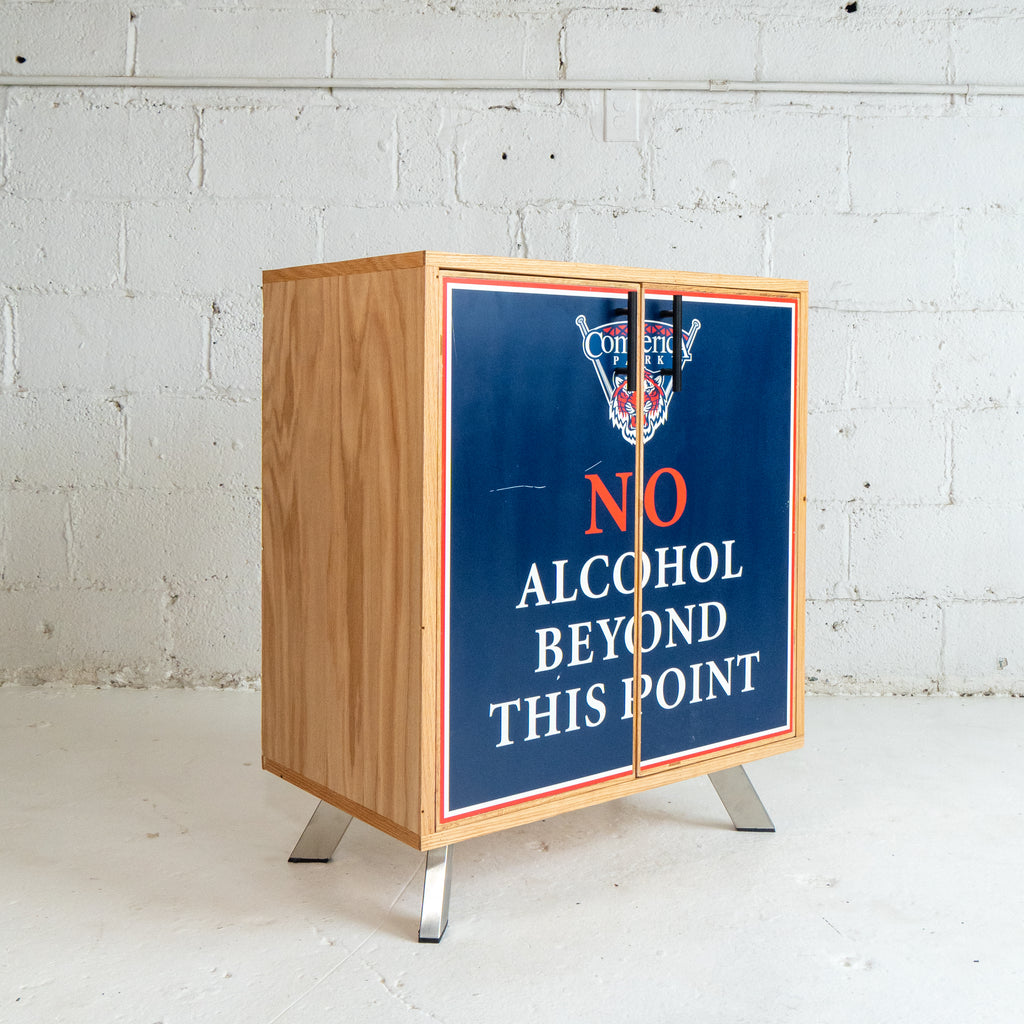 Wooden cabinet with a sign reading 'No Alcohol Beyond This Point' against a white brick wall.