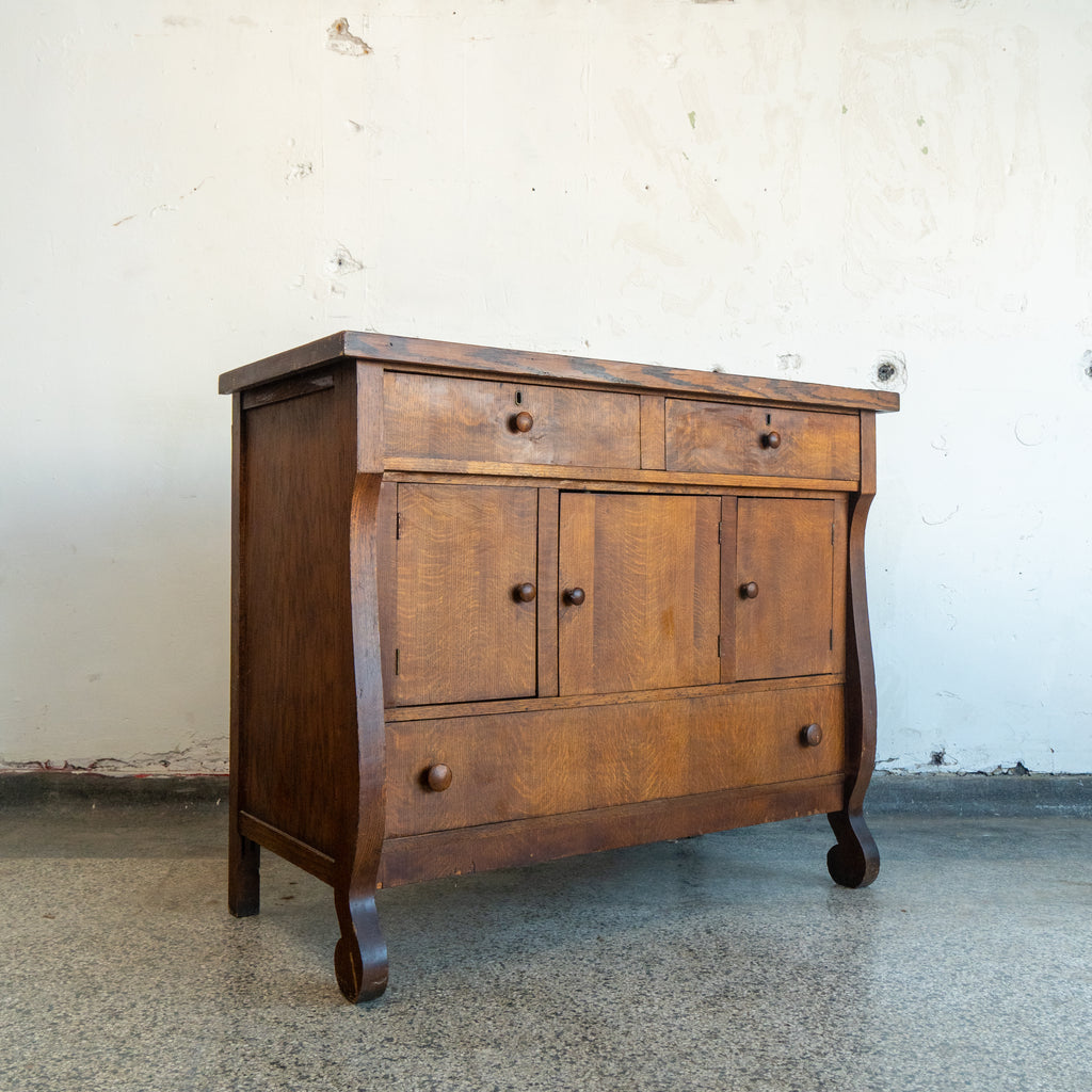 Wooden dresser with multiple drawers and doors against a plain wall. full view