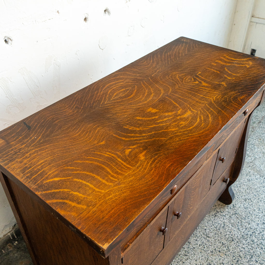 Wooden dresser with a textured surface on a speckled floor.
